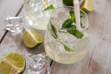 two refreshing cocktails with green ingredients in glass jugs standing on white wooden background