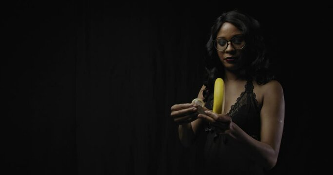 Young beautiful woman in glasses is showing how to use a condom on a banana, 4k
