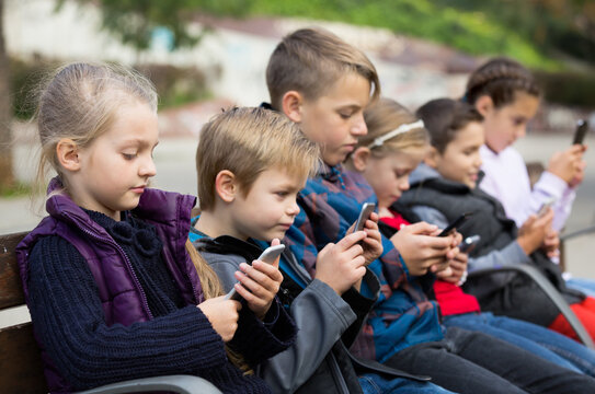 Children sitting on bench with smartphones in street
