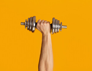Male hand lifting heavy dumbbell on orange background, closeup