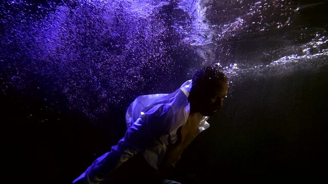 black man is diving underwater in dark deep pool, subaquatic shot of sinking persone