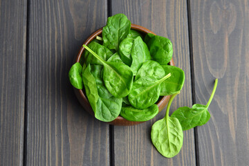 Bowl with fresh green spinach leaves over dark wooden table background. Vegan food trend. Eco-conscious concept. Top view.
