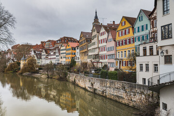 Fototapeta na wymiar Historical houses reflect on the River Neckar 's water with Saint George Church bell tower above the typical pitched roofs. Medieval architecture glimpse at the popular Neckarfront - Tubingen, Germany