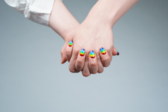 Image of woman with rainbow manicure holding hand with other woman