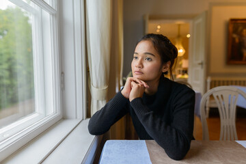 Portrait of young beautiful Asian woman looking out the window at home