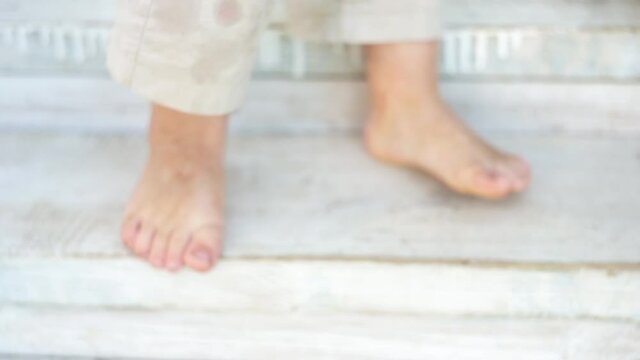 barefoot feet of a toddler stand on the painted wooden steps of a porch