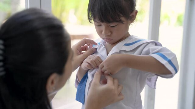 kindergarten student wearing school uniform helped by her mom in the morning. back to school preparation