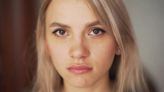 Close-up portrait of a serious face blonde girl standing in front of white wall