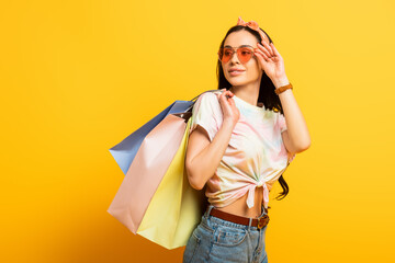 smiling stylish summer brunette girl with shopping bags looking away on yellow background
