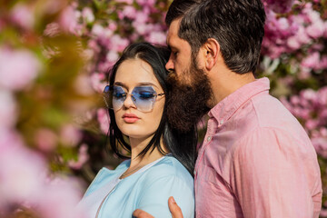 Fototapeta premium In love with spring. Tender love. Couple sakura tree background. All flowers to her. Man and pretty woman enjoying pink cherry blossom. Romantic date. Couple in love cuddling outdoors. Fashion people