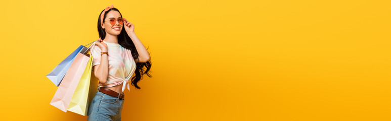 smiling stylish summer brunette girl with shopping bags on yellow background, panoramic shot © LIGHTFIELD STUDIOS