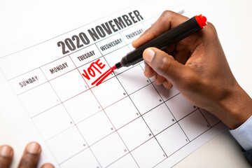 African man writing vote red text on November 2020 calendar