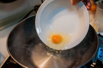 A hand-poured raw egg from a bowl into hot cooking oil in a pan