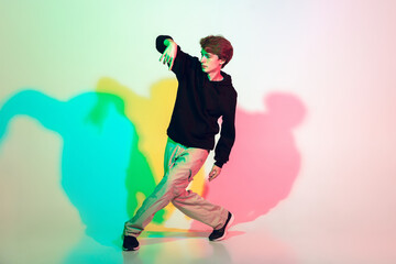 Fototapeta na wymiar Young beautiful man dancing hip-hop, street style isolated on studio background in colorful neon light. Fashion and motion, youth, music, action concept. Trendy clothes. Copyspace for ad.