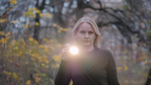 Searches in the forest - a woman with a flashlight walks through a dark forest