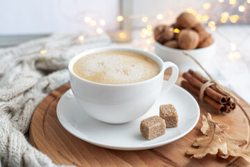 White cup with coffee, knitted scarf and garland on wooden table. Autumn mood. Cozy autumn composition. Hygge concept