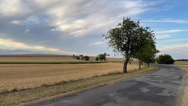 On the road between empty field after harvesting in summer evening. Czech Republic. Amazing sunset in Czech Bohemian Upland.