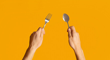 Millennial guy showing metal fork and spoon on orange background, closeup