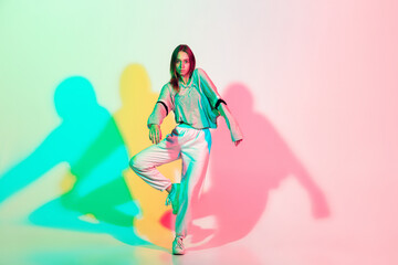 Young beautiful woman dancing hip-hop, street style isolated on studio background in colorful neon light. Fashion and motion, youth, music, action concept. Trendy clothes. Copyspace for ad.