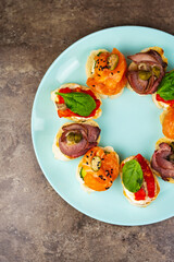 Delicious canape snacks with red fish fillet,veal meat,capers on bread served on blue plate,shot directly from above in flat lay.Tasty snack food prepared with natural ingredients for wine party