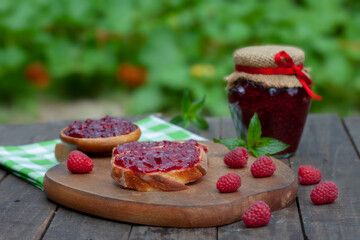 Raspberry jam with fresh raspberries and bread slices on a wooden table. Homemade marmalade, perfect for light, sweet breakfast.