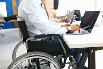 Disabled businessman sits in wheelchair in office and works at laptop. Equal rights and equal opportunities for people with disabilities concept