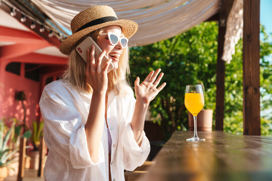 Image of joyful nice woman talking on cellphone while drinking cocktail