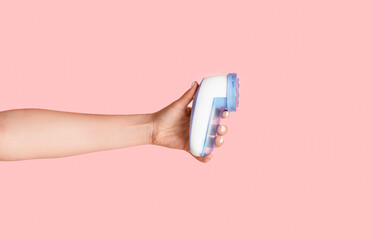 Female hand showing electric massager over pink background, closeup