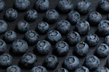 Symmetrical rows of blueberries on a black stone board. Stylish background. Berry.