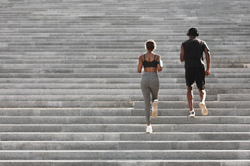 Outdoor sport. Black couple running on stairs in city park, rear view