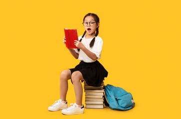 Cute School Girl Reading Book Sitting On Books, Yellow Background