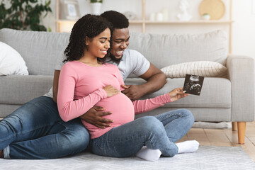 Happy black parents looking at baby ultrasound image