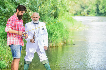 Fototapeta premium Weekend time. Fishing skills. Summer weekends or vacation. Fishing excuse drinking. Bearded man and elegant businessman fishing together. Cheers. Men relaxing nature background. Fun and relax