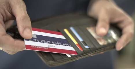 Man pulls plastic bank card with flag of Thailand out of his wallet, fictional card number