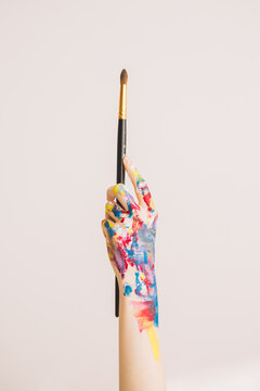 Woman's hand smeared with paints holding paintbrush. Close-up photography for ad of art school or art blog