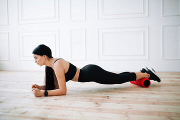 Asian woman athlete in a black top and sports leggings performs a plank exercise using a massage...