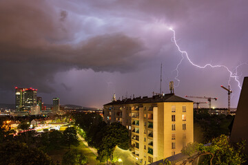 Fototapeta na wymiar Violent summer thunderstorm with enormous lightning over the Wienerberg City in Vienna with construction cranes on the right side of the picture