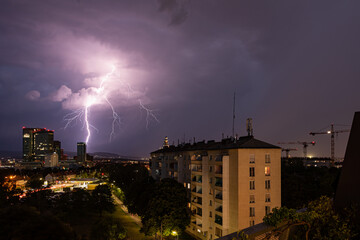 Violent summer thunderstorm with enormous lightning over the Wienerberg City in Vienna with construction cranes on the right side of the picture
