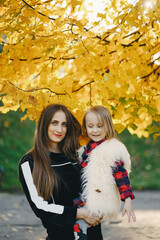 young beautiful long-haired mother in black dress walks with a little stylish daughter in the autumn city