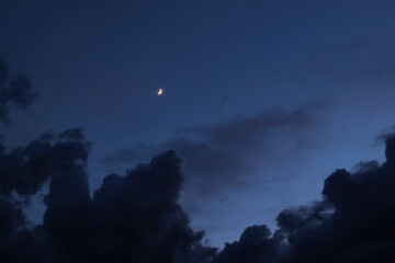 A scenic shot of the crescent moon shining in the cloudy night sky