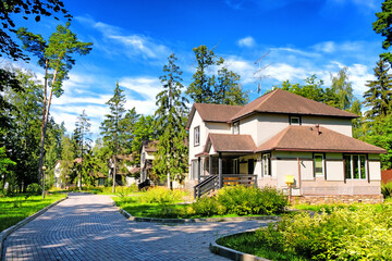 deserted house in cottage housing landscape with bricks road against trees and blue sky background. Empty street in city. Abandoned town. Unfinished construction building. Wide view