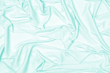 Pastel mint green silk fabric texture. Light turquoise satin cloth folds abstract background
