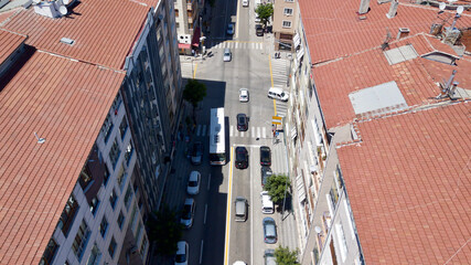 Aerial view of the crosswalk and road junction between buildings at the city center. Vehicles are waiting in red light and pedestrians are crossing the street. 