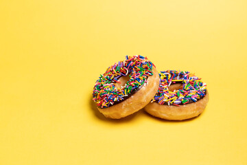 Two of chocolate frosted donuts with sprinkles on yellow background. Playful and joyful tasty sugary comfort food for customers with copy space.