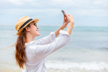 Happy young women wearing  sun glasses use mobile phones to take pictures on the beach While traveling.