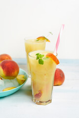 peach refreshing juice cocktail in a glass with ice and pieces of fruit and mint in the summer. top view on a light background