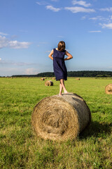 Naklejka na ściany i meble A cheerful girl dances on a haystack. The girl has fun and has a good time in nature. The girl is happy in nature. Haystack down the middle of the field.