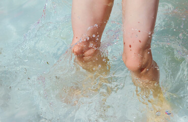 close-up - feet of a five-year-old boy who jumps, plays in the water in a children's inflatable pool, splashes water