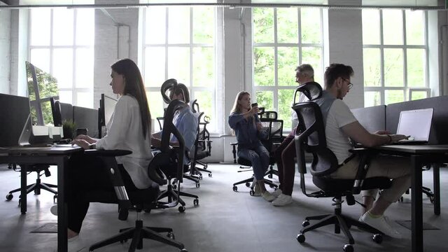 Business people office workers group using pc working talking in big modern coworking space, employees team women men sitting at desks with computers in modern enterprise interior at workplace