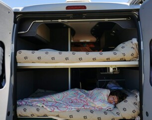 Child sleeps very comfortably in one of the bunks of a camper van. Holidays with outdoors